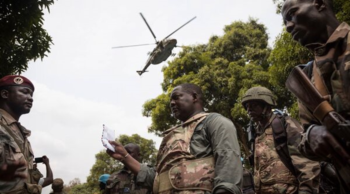 CAR Prime Minister Firmin Ngrébada (centre) talks to troops as a Russian Mi-8AMTSh helicopter flies overhead on the road between Boali and Bangui on 10 January.