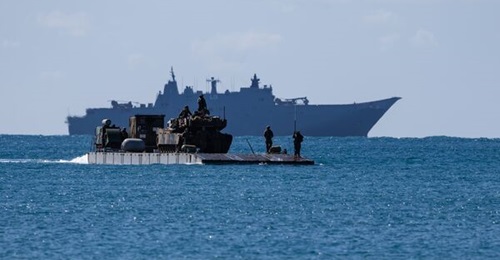 An M1A1 Abrams main battle tank is transported via a mexefloat to the beach head with HMAS 
        
         in the background during Exercise 'Sea Raider' 2023.