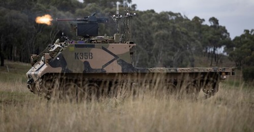 An Australian Army M113AS4 armoured logistics vehicle, fitted with optionally crewed combat vehicle technology and a remote weapon station, fires from a support-by-fire position during a human-machine team exercise at Puckapunyal Military Area.