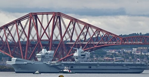 The Royal Navy aircraft carrier HMS
        
         passes under the Forth Bridge after leaving Babcock's Rosyth Dockyard, where it has been undergoing repairs, on 22 July 2024.