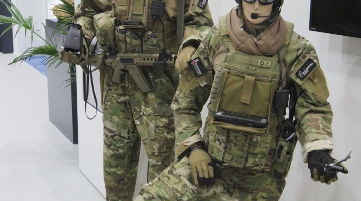 The Rheinmetall Canada Argus soldier system displayed at IDEX 19 with the baseline Saab Linux display (left) and the chest-mounted Windows tablet for commanders (right). The antenna for the MPU5 is visible over the left-hand model's left shoulder.