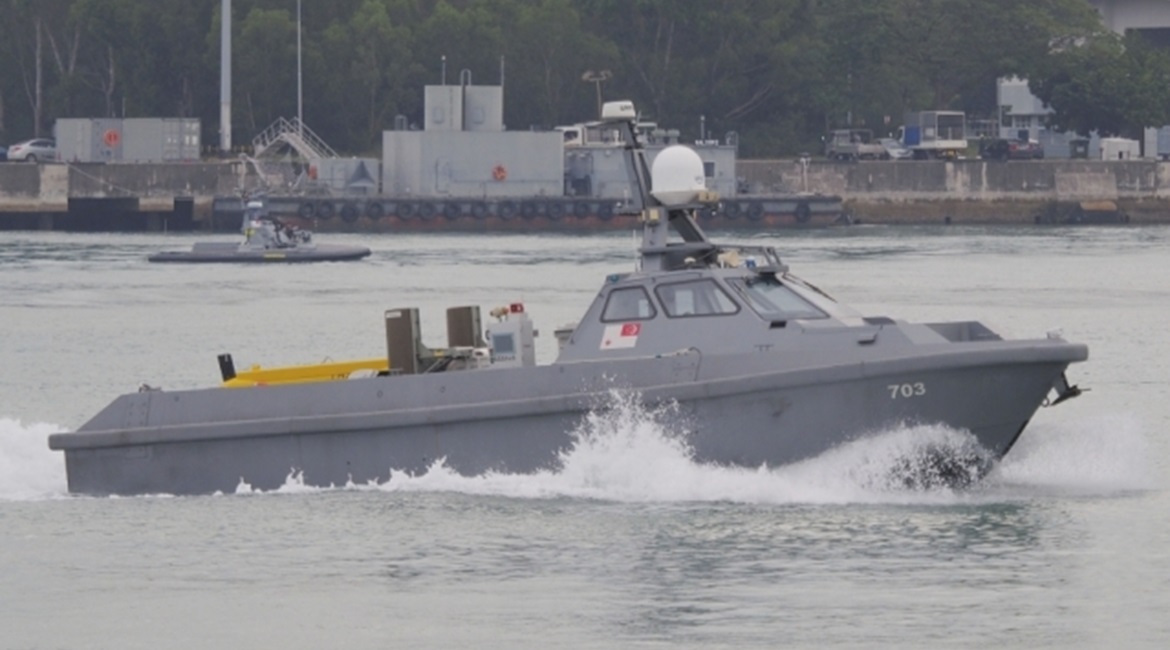 The mine detection variant of the Venus 16 unmanned surface vehicle leaving harbour for sea trials. The in-service Protector unmanned surface vehicle can be seen in the background.