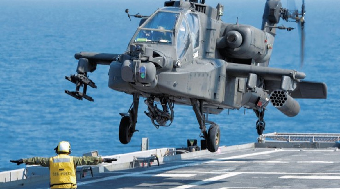 A US Army AH-64D Apache helicopter prepares to land aboard USS 
        
         during an exercise. With an increasing emphasis on maritime operations for the helicopter, the service is to fit an emergency underwater crew escape system.