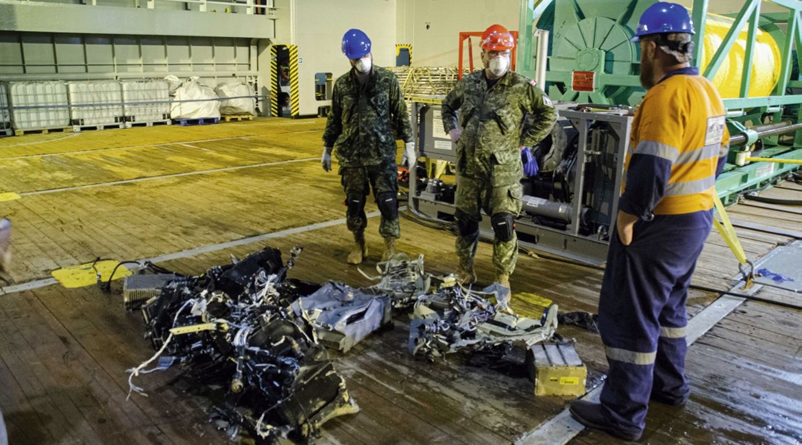 Canadian Armed Forces members and EDT Hercules personnel inspect recovered parts of CH-148 Cyclone on 31 May 2020 during recovery operations for the aircraft.