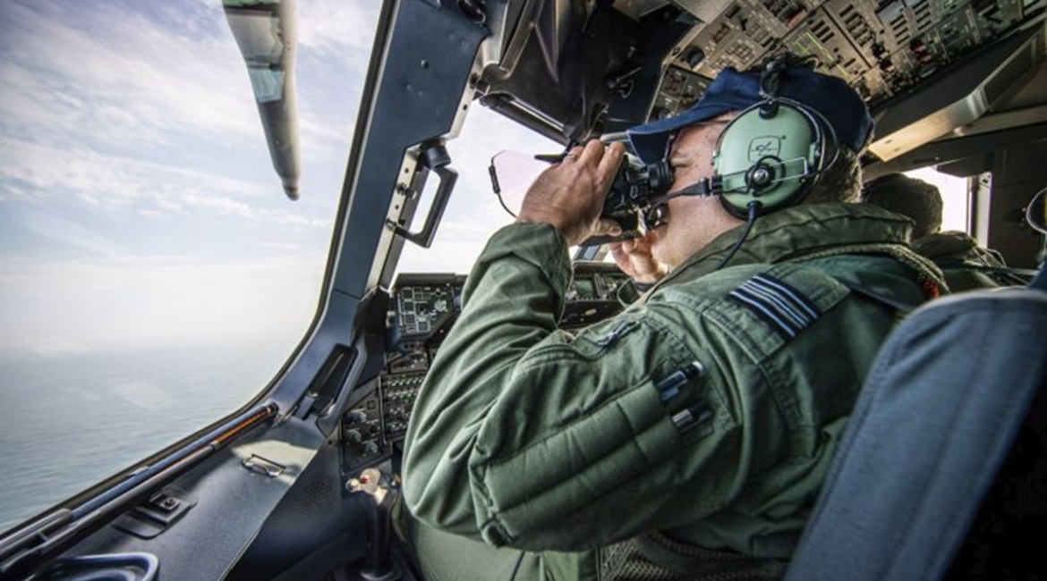 An RAF A400M crew member using binoculars to scan the English Channel for migrant boats.