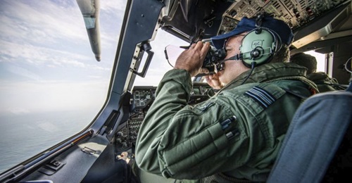 An RAF A400M crew member using binoculars to scan the English Channel for migrant boats.