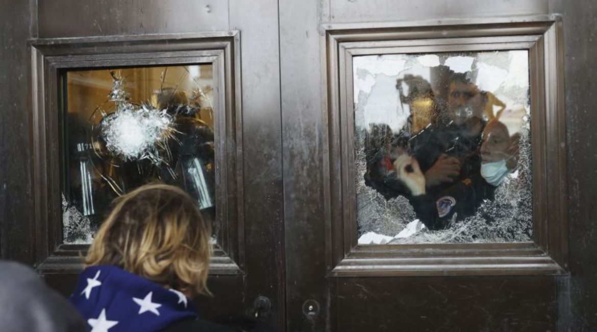 A photograph depicting pro-Trump protesters attempting to enter the Capitol Building, glass on the doors of which has been damaged.