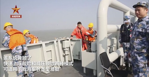 A screengrab from CCTV footage released on 2 January showing submariner boarding a support vessel after recovery from a life raft, wearing new escape suit. The image also shows a yellow hood inflation connector.