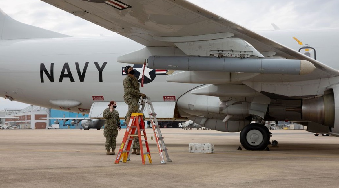 A member of the Air Test and Evaluation Squadron (VX) 20 puts a pod-mounted radio frequency countermeasure system on a P-8A Poseidon.